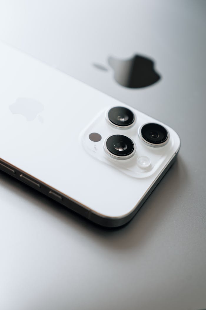 White smartphone with triple cameras lies atop a sleek laptop.